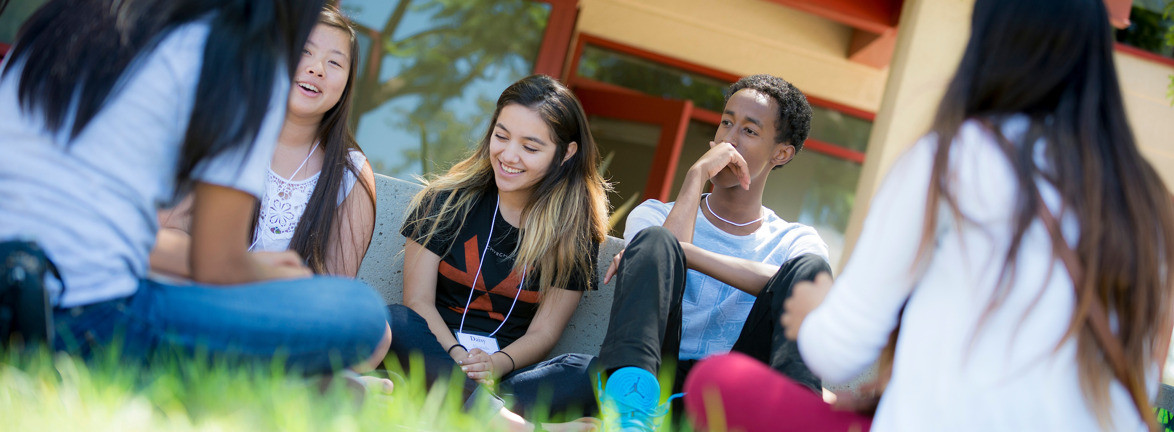 five students sitting in grass, talking to each other